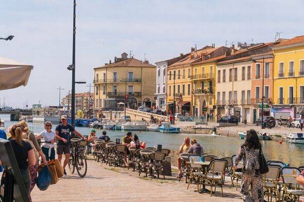 Sète, France, main canal through the city with people walking by, boats at dock