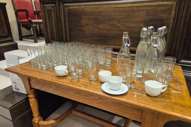 Bottles of tap water, glasses and cups with saucers on a desk at council meeting