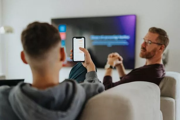 Teenage boy with mobile phone talking to father while sitting in living room