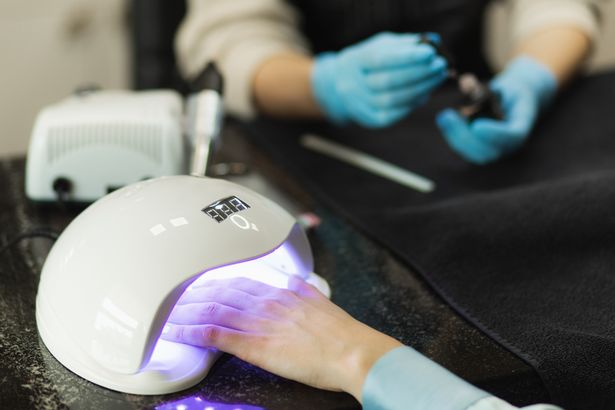 Closeup view of female hands with fresh beautiful pink modern gel polish manicure. Woman puts hand into led uv lamp for curing top cover of nailpolish. Professional manicure with gel polish in beauty salon.