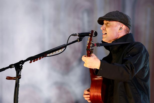 Gerry performs on stage smiling in a hat and coat