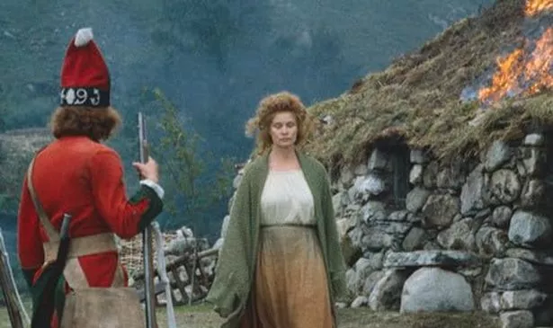 A woman in green and white walks past a burning building 