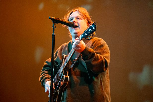 Lewis Capaldi performs during his 2025 tour wearing green jumper and playing guitar