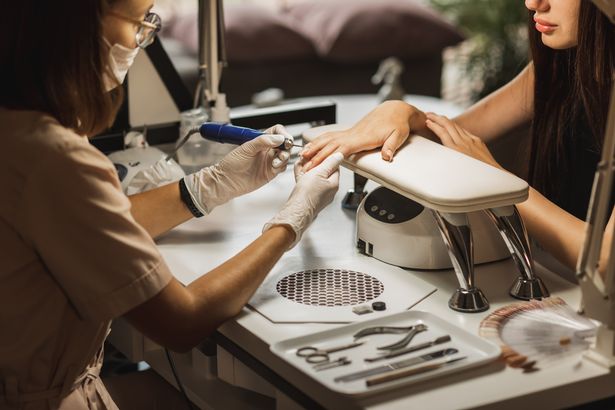 Manicure master in gloves with cuticle remover device in beauty salon. Master using electric machine to remove the nail polish during manicure in the salon. Professional manicure tool. Concept of body care.