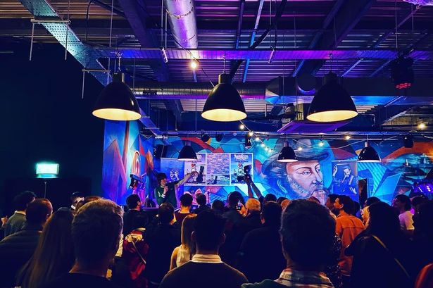 Several people looking at a person perform on the stage. People are cheering, and the general lighting over the picture is blue