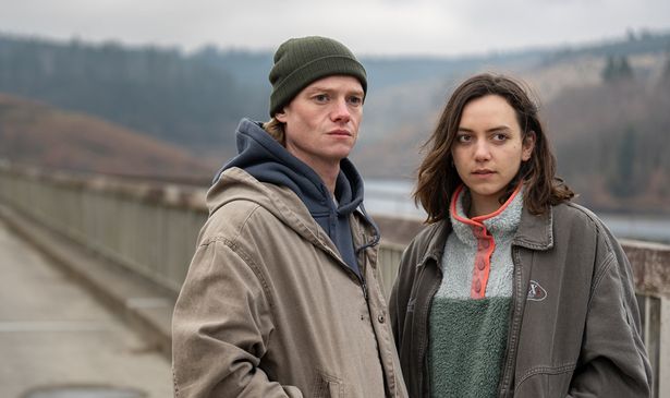 A young man and a woman stand on a bridge 