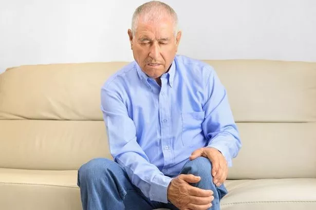 An older man is holding his knee in pain.