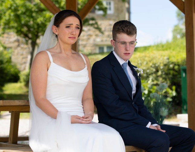 Gabby and Arthur sitting on a bench in Emmerdale. Gabby is wearing her wedding dress and Arthur has a suit on