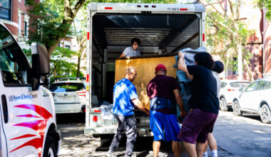 Several people work to move a large piece of furniture out of the back of a U-Haul truck.