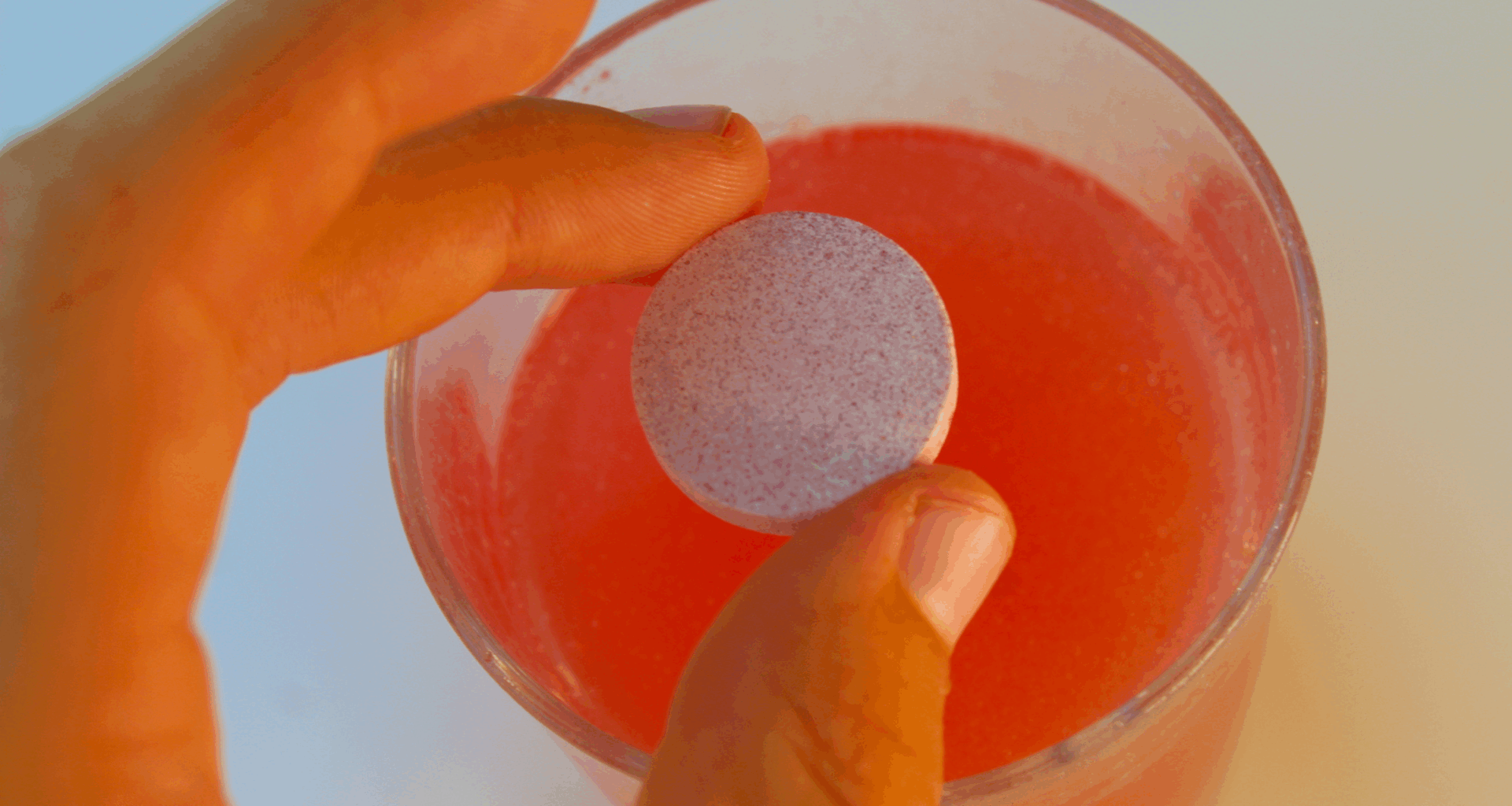 a person's hand dropping an electrolyte tab into a glass of water