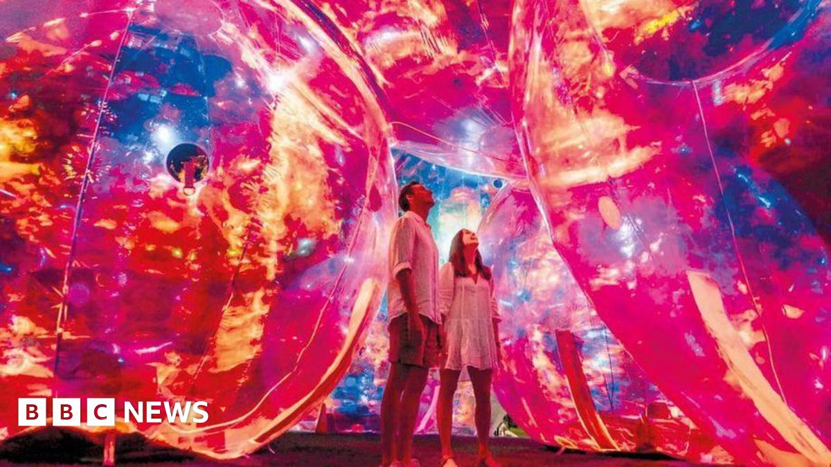 One of the installations at a previous Leeds Light Night festival. Two people stare up at glowing red and yellow spheres surrounding them.