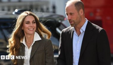 Shoulder crop of William and Catherine. William is wearing a black blazer and light blue shirt. Catherine is wearing a tweed-style jacket and white shirt. She has blonde hair. Both are smiling and posing outside the museum.