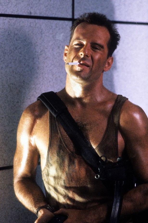 Bruce Willis in a brown vest and with a cigarette in his mouth in a scene from Die Hard.