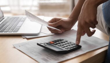 African woman holding in hand paper bills bank receipt using calculator on table calculate debt loan tax cost to pay manage finances concept doing accounting paperwork budget analysis, close up view.