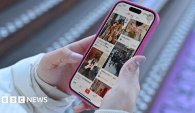 A close-up picture of a woman holding a phone with Chinese social media app Xiaohongshu loaded on the screen