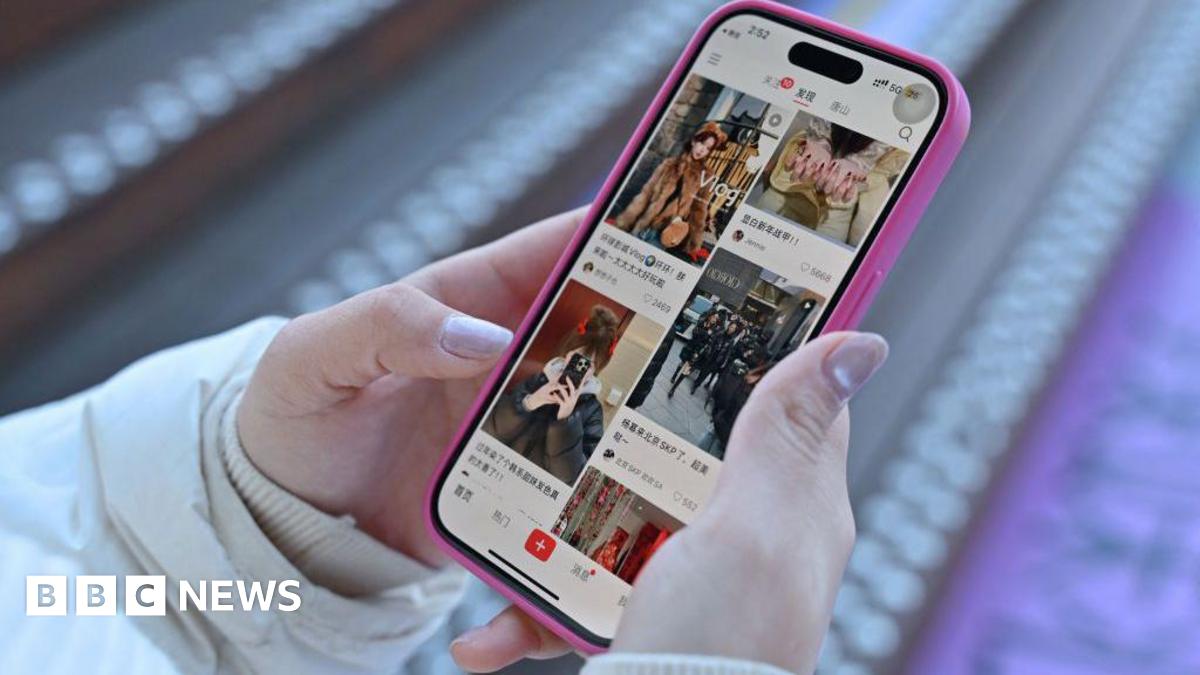A close-up picture of a woman holding a phone with Chinese social media app Xiaohongshu loaded on the screen
