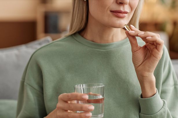 Minimal close up of adult woman taking vitamin pill and holding glass of water at home copy space