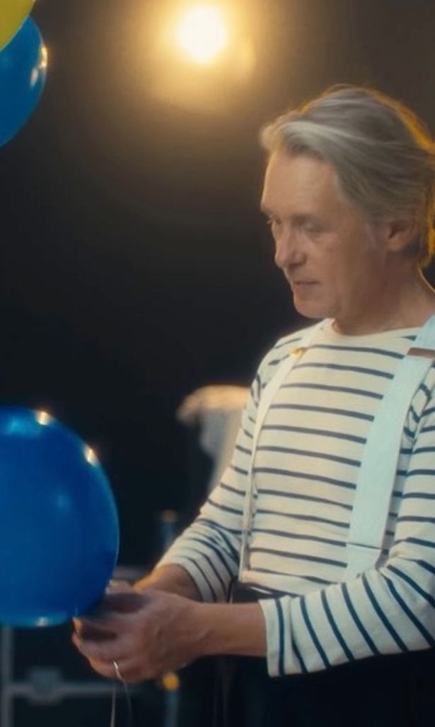 Mark Owen in a striped top and dark trousers holding a balloon