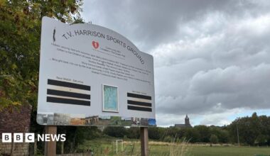A sign which reads T.V. Harrison Sports Ground with a football field in the background.