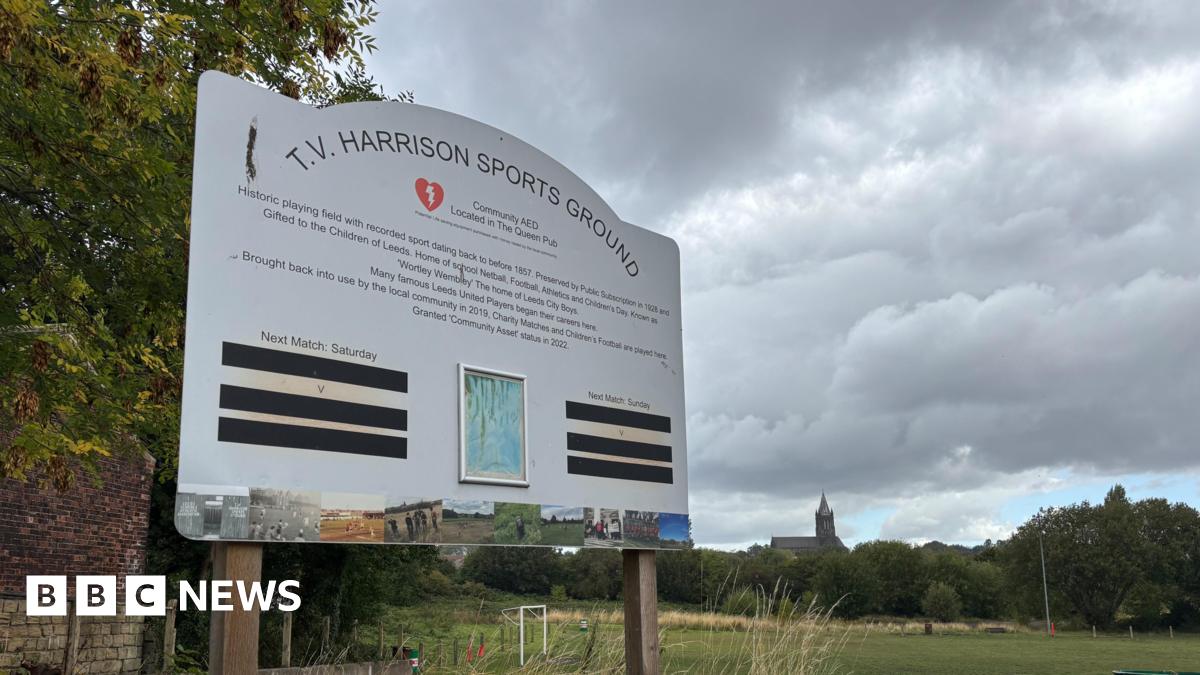 A sign which reads T.V. Harrison Sports Ground with a football field in the background.