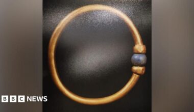 The Bracelet is gold and adorned with a blue, round bead.