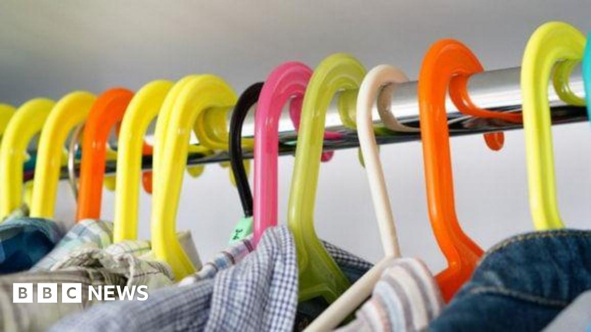 Different coloured clothes hangers on a metal pole. There are flannel tops on the hangers. The background is grey.