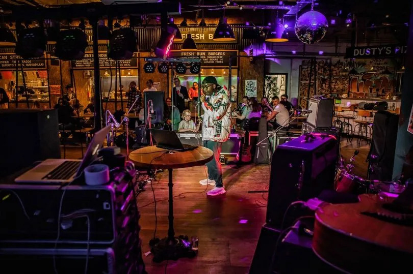 SZWÉ performing at last year’s Fringe launch at Founders and Co. He is standing in the middle of the stage holding a mic in his hand.