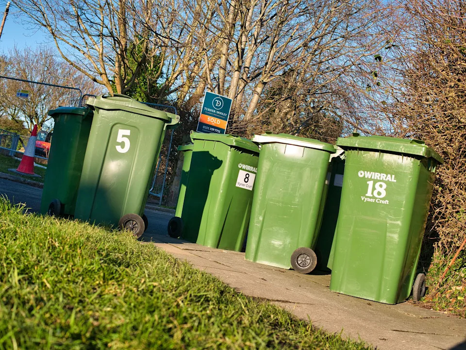Many green plastic recycling - refuse bins blocking the pavement in an urban area in Wirral on a sunny day in winter.