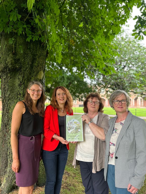 National Trust director Heather McLachlan centre of photo wearing a red jacket. She had shoulder length ginger hair and is stadning next to a large tree. 
