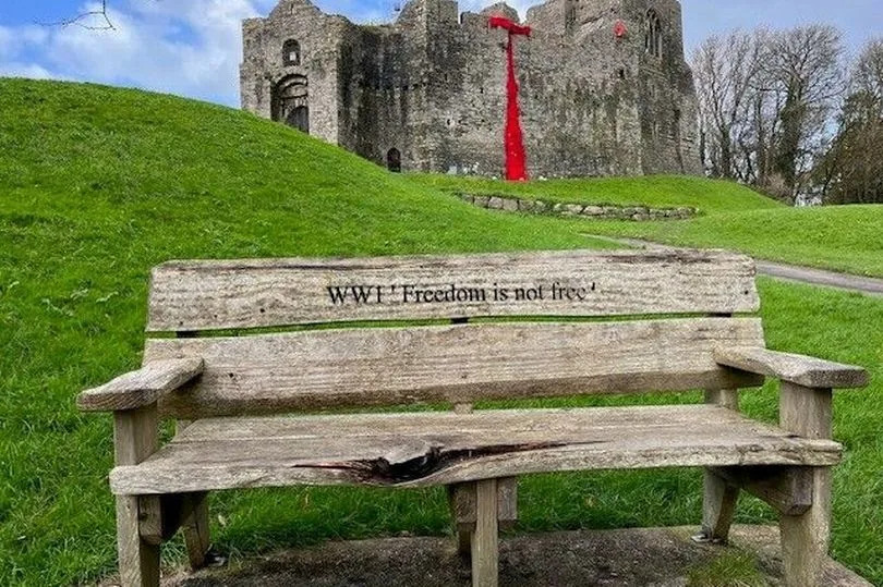 A wooden bench seen in the foreground, as Oystermouth Castle is visible in the background