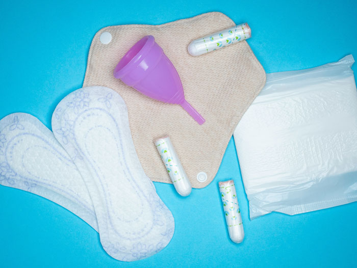 Menstrual hygiene products including pads, tampons, and a menstrual cup on a blue background representing the girl’s health context.