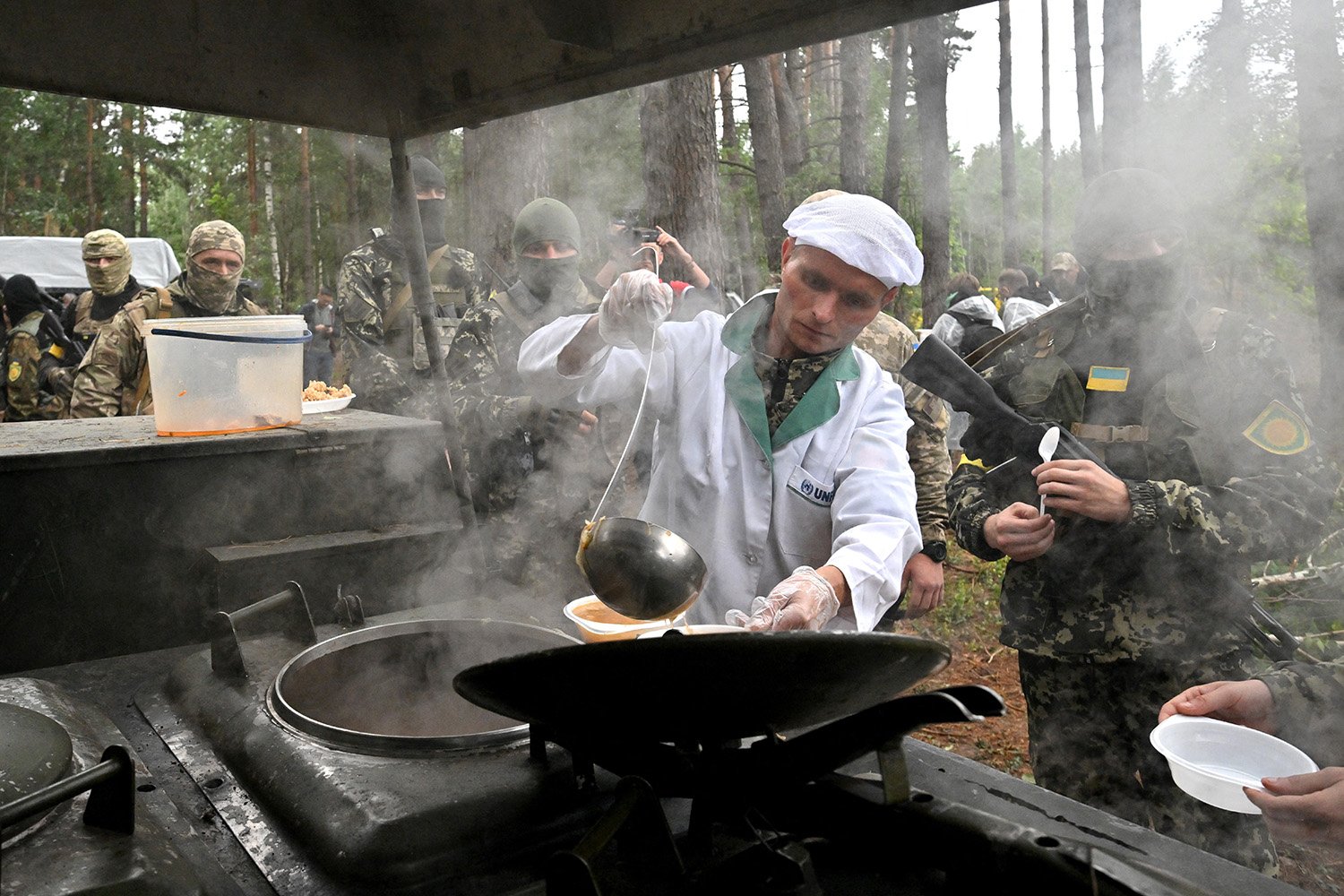 Ukrainian soldiers in the woods queue for food as it is served.