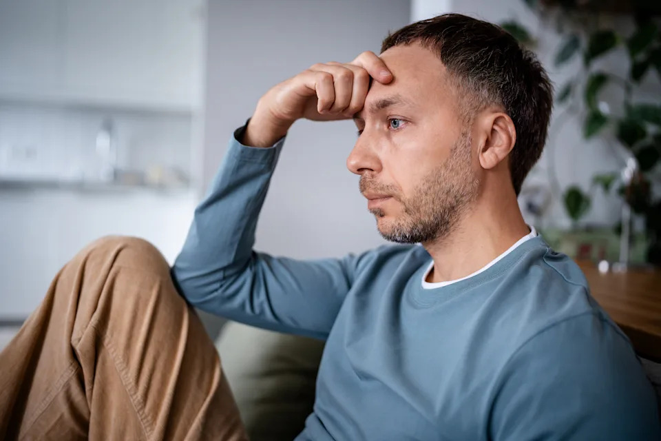 Emotionless man staring blankly ahead on couch. Psychological exhaustion from prolonged stress, burnout male depression, inner emptiness and disconnection from reality, brain fog apathy and melancholy