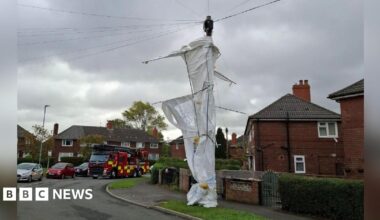 A large white canvas tent wrapped around a telegraph pole on a suburban street. A fire engine can be seen on the road in the background.