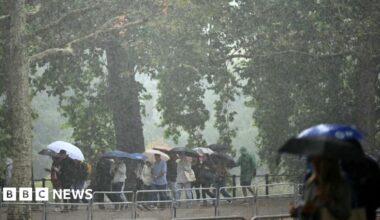 People walk with umbrellas as they're hit by rain and heavy winds