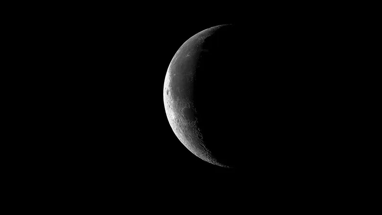 A crescent moon in space with the rest hidden in shadow