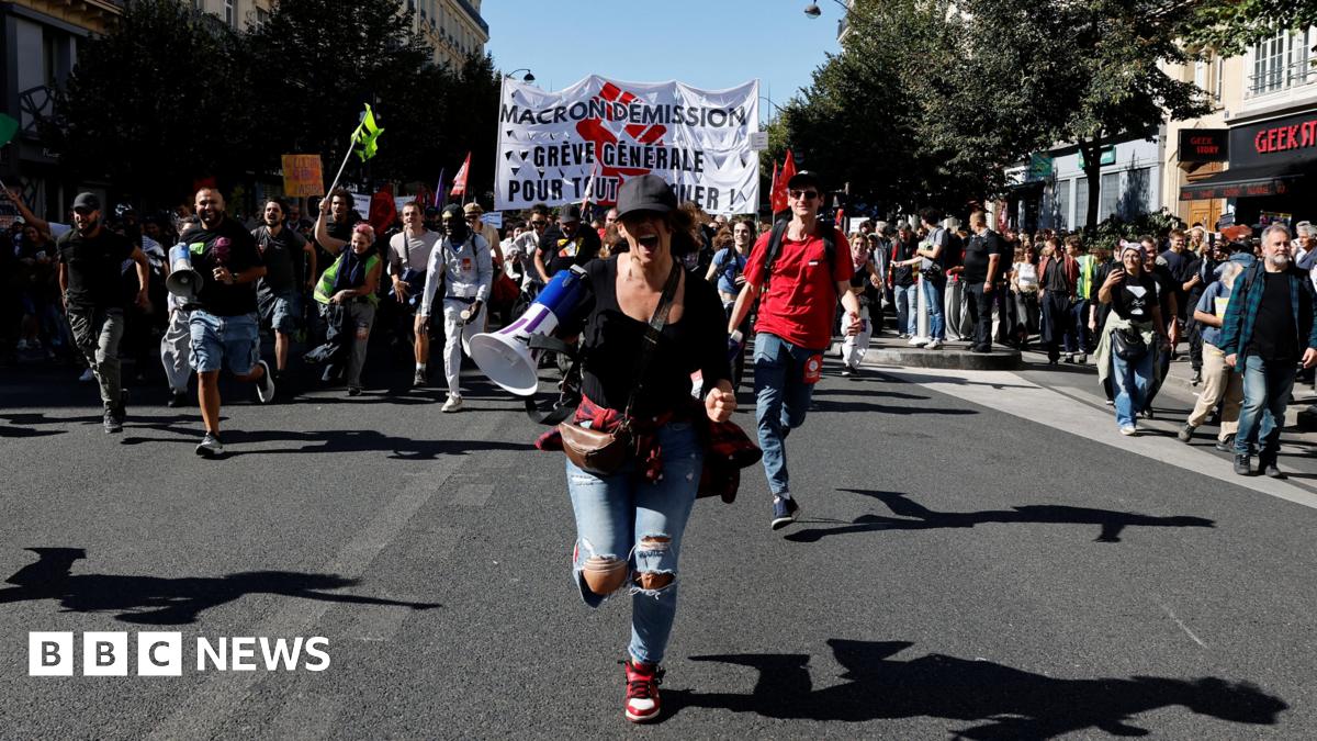 A woman with a megaphone runs towards the camera as the crowd approaches behind her