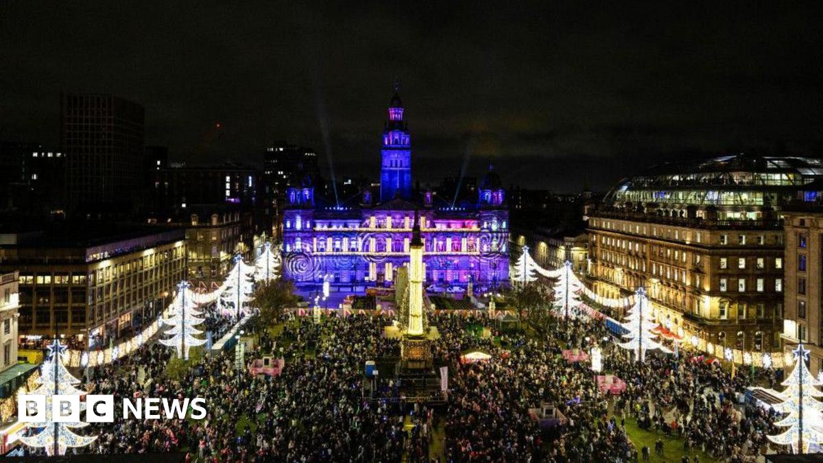 A view from high up, looking down on a city square. Christmas decorations are all around it, along with crowds of people, while the city chambers building behind the square is lit up in purple.