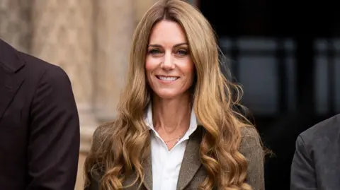 PA Media Kate, who has long curly dark blonde hair, seen smiling at cameras 