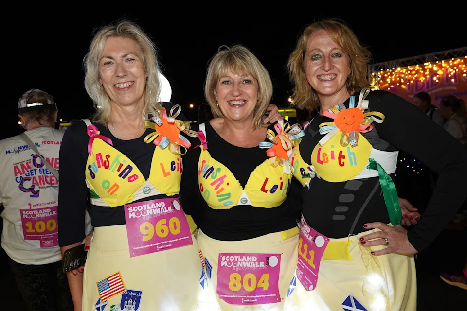 Three women in yellow bras with the words Sunshine on Leith written on top of them smile into the camera