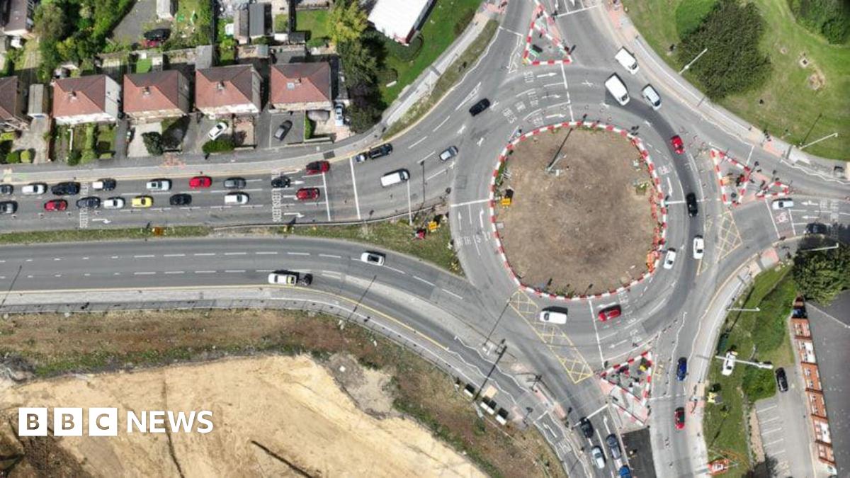An aerial view of a roundabout on a busy road junction in Pudsey. The road has red and white barriers surrounding it, indicating improvement work is taking place.