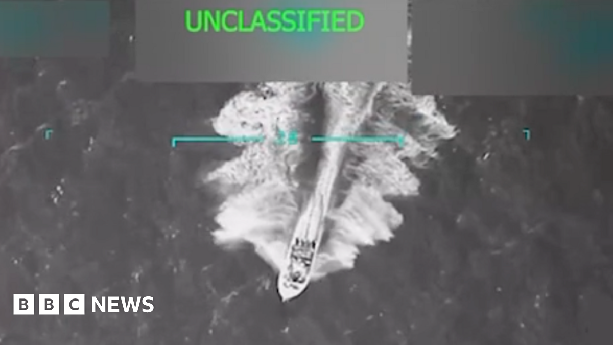 A grainy aerial video still shows a motor boat speeding across choppy waters