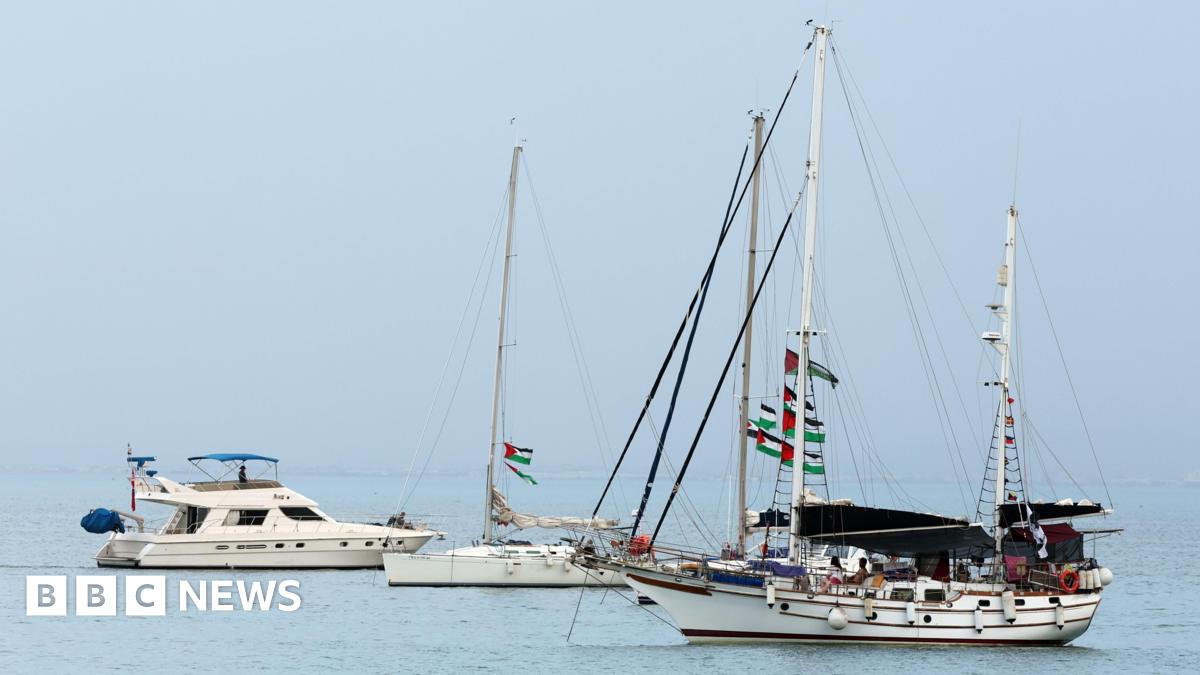 Three sailing boats are seen anchored in turquoise waters, with Palestinian flags strung through the rigging and masts of the vessels.