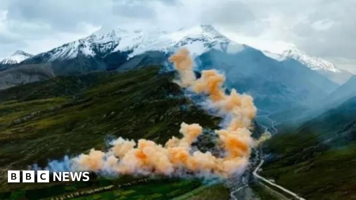 Clouds of colourful smoke rise from a fireworks display over hills, with the snow-capped peaks of the Himalayas in the distance