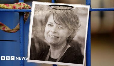 A printed black and white photograph of Ruth Perry fixed to a blue-coloured fence. Mrs Perry is smiling in the photo.