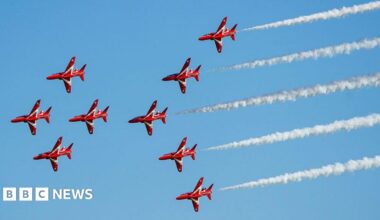 The famous Red Arrows jets - nine in total - fly from right to left across the picture in close formation with white smoke billowing from five of them at the back