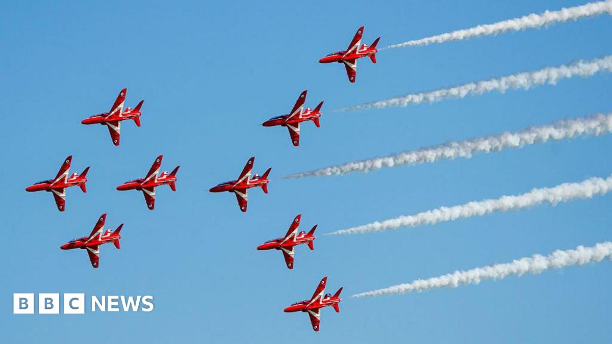 The famous Red Arrows jets - nine in total - fly from right to left across the picture in close formation with white smoke billowing from five of them at the back