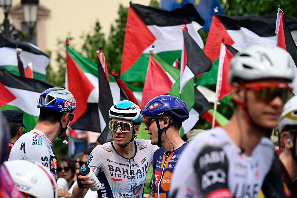 Pro-Palestinian protesters wave flags as riders await the start of the 15th stage of the Vuelta a Espana cycling tour, a 167 km race between A Veiga/Vegadeo and Monforte de Lemos, on September 7, 2025. (Photo by Miguel RIOPA / AFP)