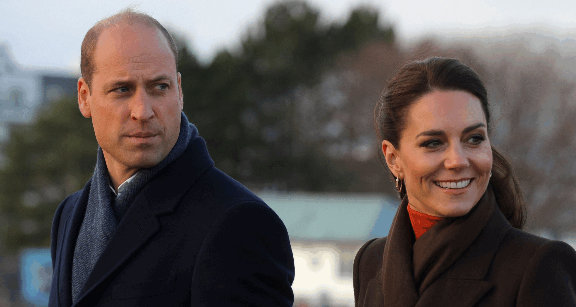Kate Middleton wearing a brown coat and smiling next to Prince William