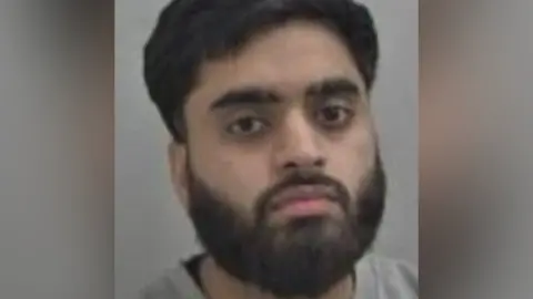West Mercia Police Anayat Ur-Rehman is seen in a police mugshot. He has a black beard and moustache and black hair.